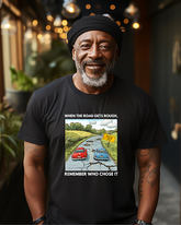 A man wearing a black t-shirt with text and an illustration on it, standing in a room with a street scene in the background.