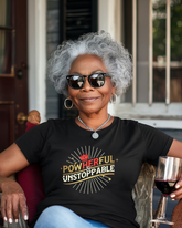 Woman wearing a black t-shirt with motivational text, sitting outdoors with a glass of wine.