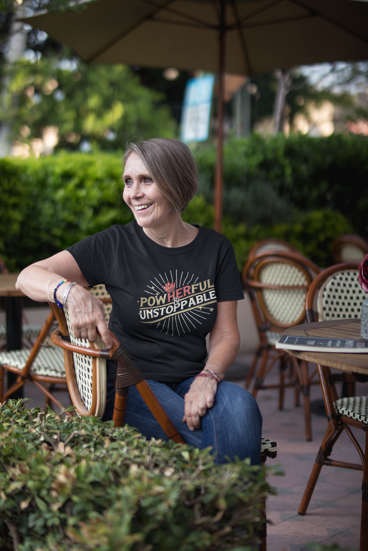 Woman sitting outdoors at a cafe with an umbrella and greenery in the background