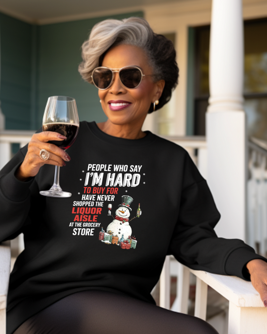 An older woman sitting on a porch swing wearing sunglasses and a black sweatshirt with a Christmas-themed design, including a snowman and text.