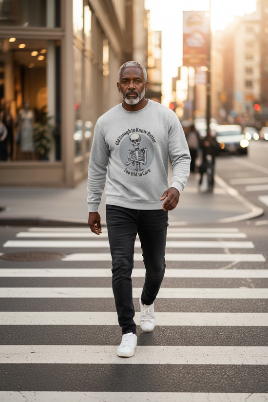 Man walking on a crosswalk wearing a gray sweatshirt with a graphic design.